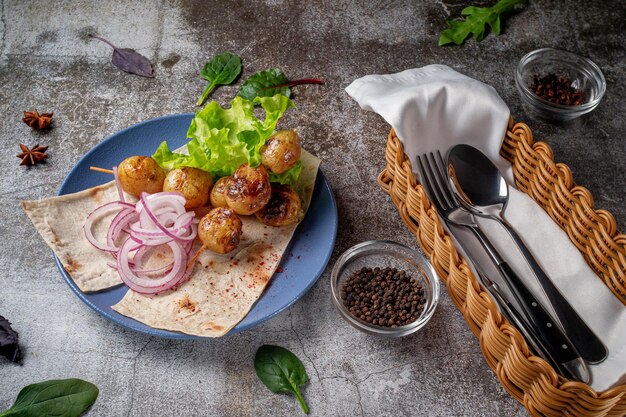 Ein Gericht aus der Speisekarte eines Restaurants servieren. Gegrillte Ofenkartoffeln im Landhausstil mit Fladenbrot, Kräutern und Zwiebeln auf blauem Teller vor grauem Steintisch