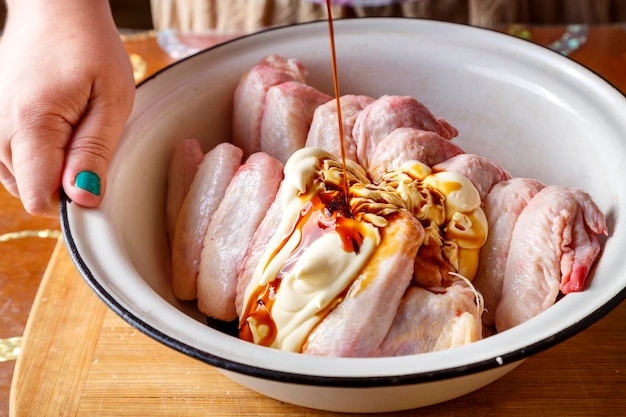 Ein Gericht mit frischen rohen Flügeln auf einem Holztisch wird mit Sojasauce gegossen
