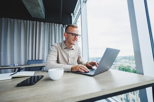 Ein Geschäftsmann arbeitet an einem Laptop, ein Manager sitzt an einem Tisch im Büro, arbeitet an einem Laptop