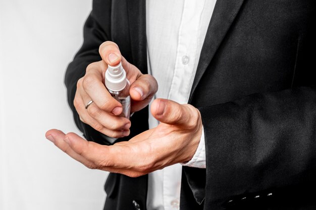Ein Geschäftsmann im Business-Anzug sprüht Alkohol-Antiseptika aus einer Sprühflasche auf seine Hand