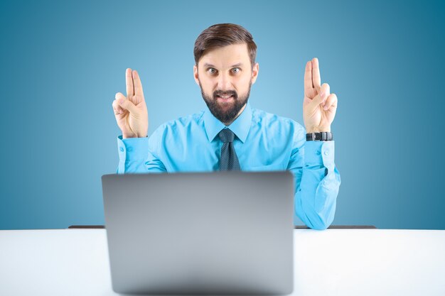 Ein Geschäftsmann in einem blauen Hemd hebt die Hände und zeigt zwei Finger, einen bärtigen Mann im Büro am Computer