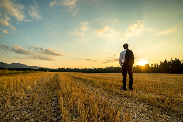 Ein Geschäftsmann in elegantem Anzug mit seiner Jacke über der Schulter steht in einem gemähten Weizenfeld