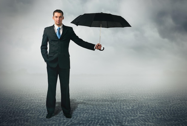 Ein Geschäftsmann mit einem Regenschirm steht vor einem bewölkten Hintergrund