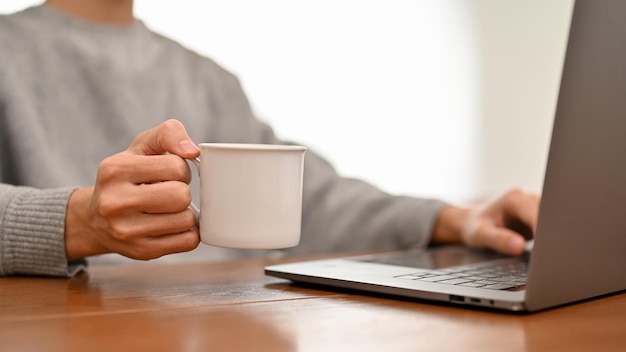 Ein Geschäftsmann oder männlicher Student, der mit einem Laptop arbeitet, während er Kaffee zuschneidet