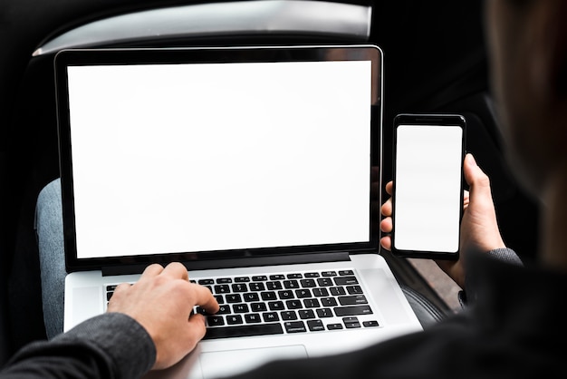 Ein Geschäftsmann unter Verwendung des Laptops und des Handys mit leerem weißem Bildschirm