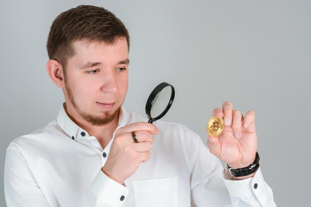 Ein Geschäftsmann untersucht eine Bitcoin-Goldmünze mit einer Lupe