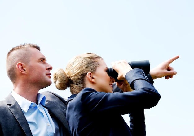 Foto ein geschäftsmann zeigt, während eine geschäftsfrau durch ein fernglas gegen einen klaren himmel schaut