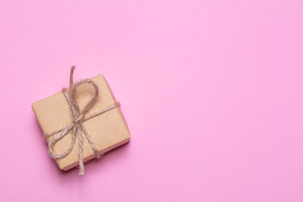 Ein Geschenk, das in Kraftpapier auf einem rosa Hintergrund eingewickelt wird. Blick von oben, flaches Design.