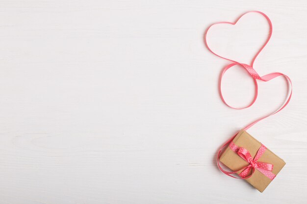 Ein Geschenk des Kraftpapiers und des rosa Bandes auf einem weißen Holztisch