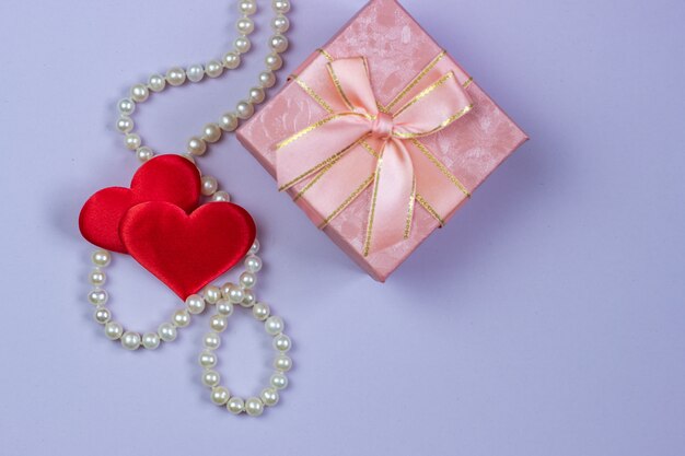 Ein Geschenk in einem rosa Kasten mit Perlen und Valentinsgrüßen auf einem purpurroten Hintergrund.