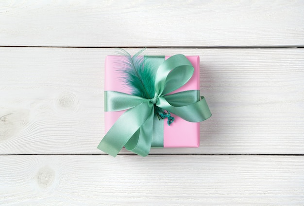 Ein Geschenk in einer rosa Packung mit einem Minzband und einer Feder auf einem weißen hölzernen Hintergrund.