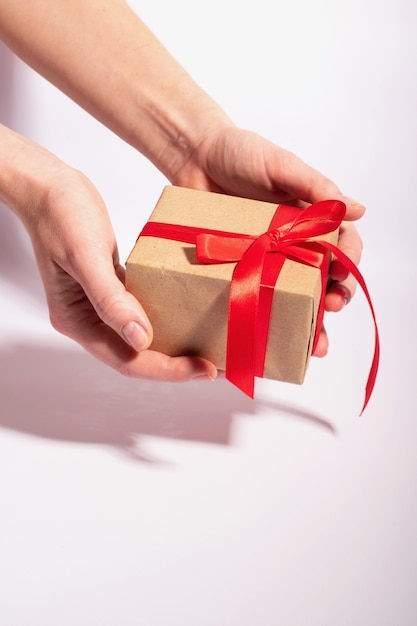 Ein Geschenk mit einem roten Band in den Händen der Frau auf einem weißen Hintergrund