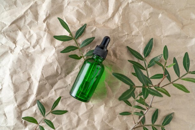 Ein Gesichtsserum oder ätherisches Öl in einer grünen Tropfflasche, die auf einem beigen Bastelpapierhintergrund liegt