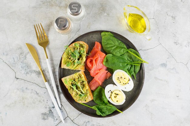 Ein gesundes Frühstück mit zwei Sandwiches mit gekochtem Avocado-Ei und Lachs auf grauem Hintergrund