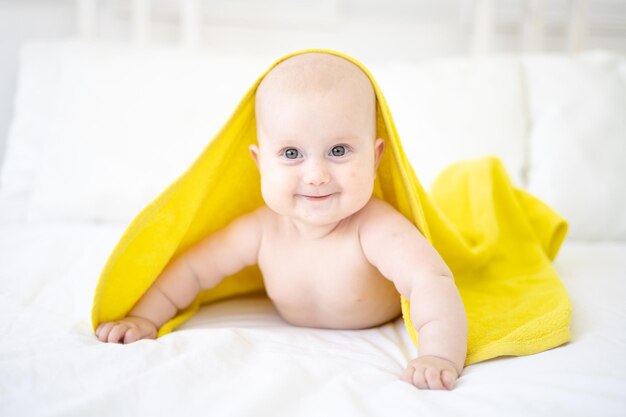 Ein gesundes, glückliches, süßes Baby liegt auf dem Bauch, nachdem es in einem Handtuch gebadet und gelächelt hat