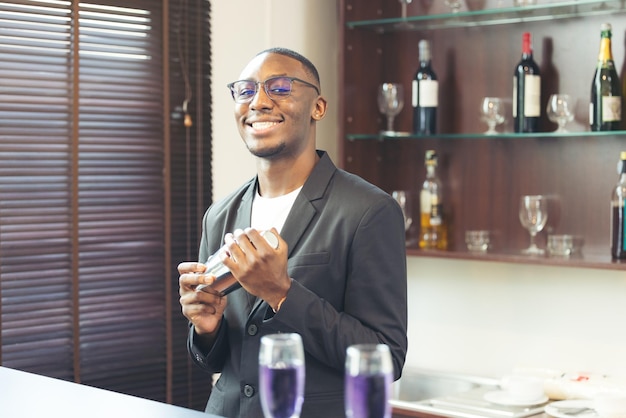 Ein Getränk zubereiten, lächelt ein schwarzer, gutaussehender Barkeeper in die Kamera