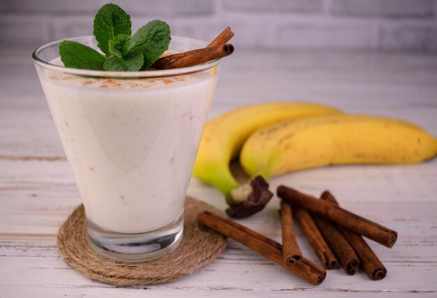 Ein Glas Bananen-Zimt-Smoothie auf weißem Holzhintergrund