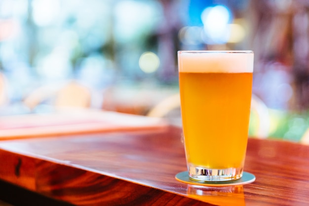 Ein Glas Bier vom Fass mit Schaum auf hölzernem Zähler mit Unschärfe und bokeh Hintergrund.