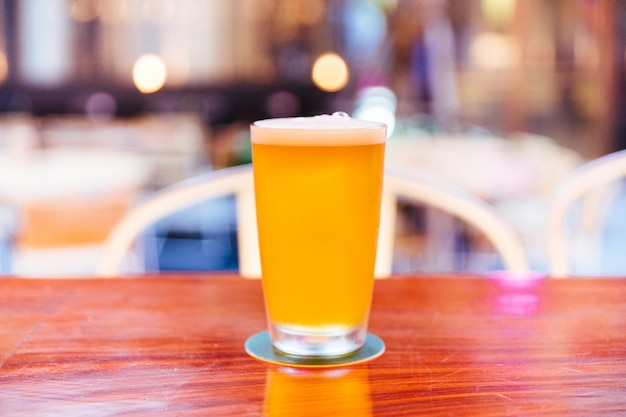 Ein Glas Bier vom Fass mit Schaum auf hölzernem Zähler mit Unschärfe und bokeh Hintergrund.