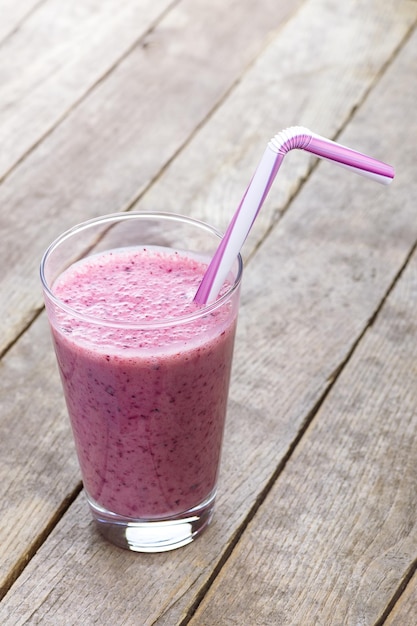 ein Glas Blaubeer-Smoothie mit Stroh auf einem Holztisch