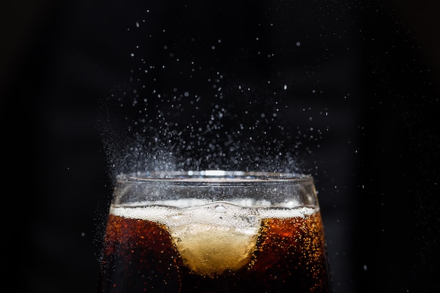 Ein Glas Cola-Getränk mit einem Salz. an einer schwarzen Wand.