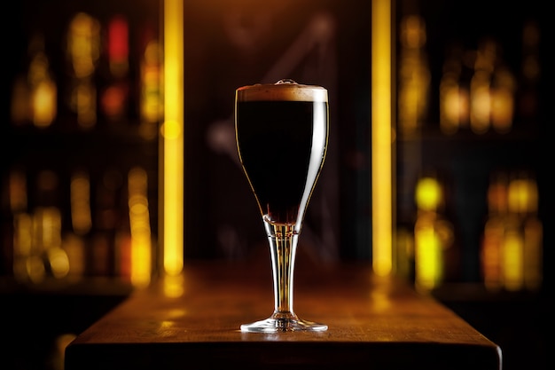 Ein Glas dunkles Bier auf einem dünnen Bein in einer Bar.