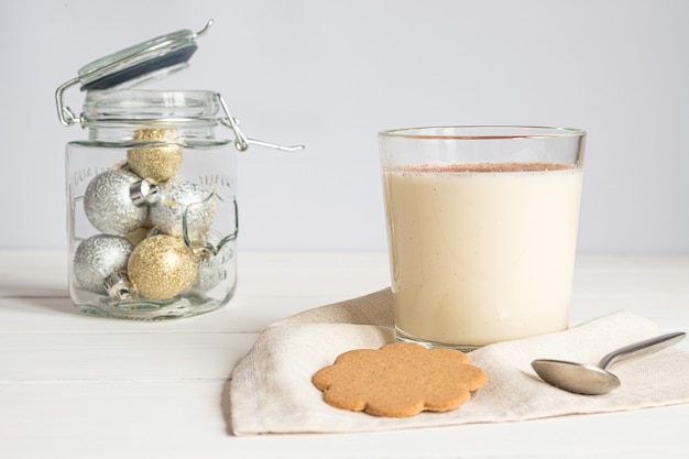 Ein Glas Eierlikör und Weihnachtsschmuck auf grauem Hintergrund