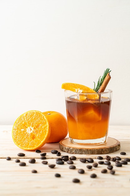 Ein Glas eisgekühlter Americano-Schwarzkaffee und eine Schicht Orangen- und Zitronensaft, dekoriert mit Rosmarin und Zimt auf Holzhintergrund