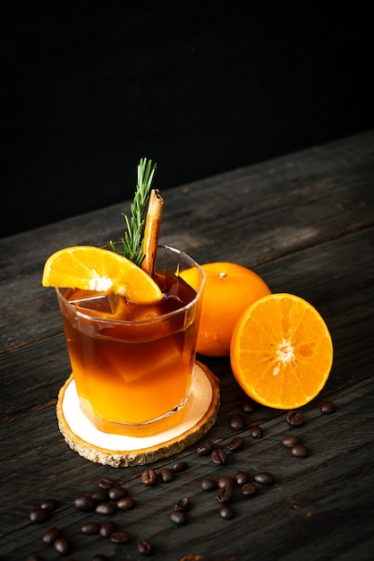 Ein Glas eisgekühlter Americano-Schwarzkaffee und eine Schicht Orangen- und Zitronensaft, dekoriert mit Rosmarin und Zimt