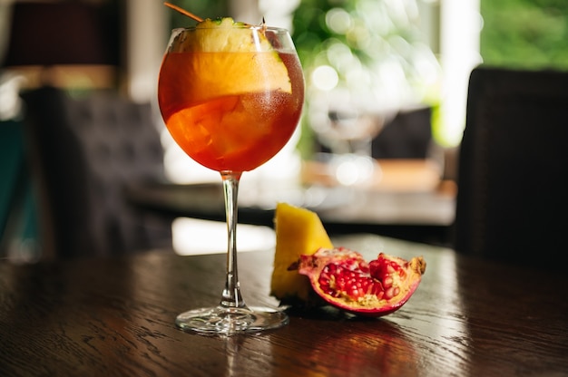 Ein Glas eiskalter Aperol-Spritz-Cocktail, serviert in einem Weinglas mit Ananas und Granat, auf einen Tisch im Restaurant gestellt