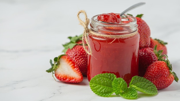 ein Glas Erdbeermarmelade neben einem Erdbeerkrug.