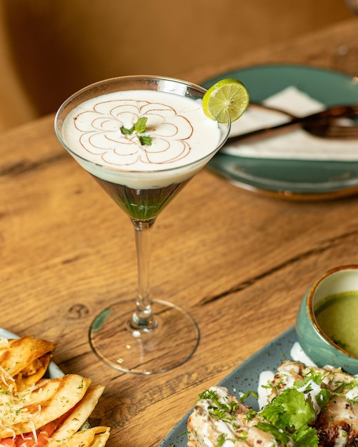 Ein Glas Essen mit einem grünen Getränk auf einem Tisch neben Tellern mit Essen.