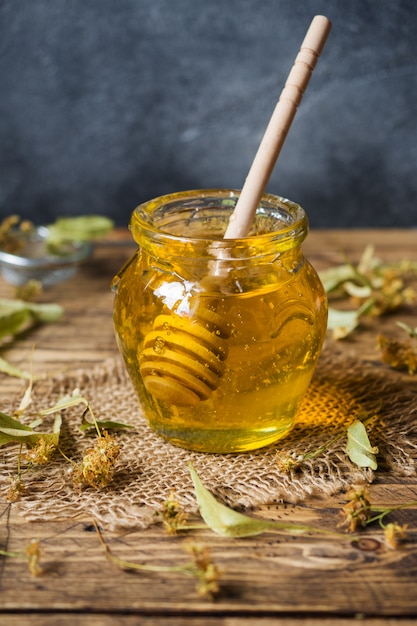 Ein Glas flüssiger Honig aus Lindenblüten und ein Stab mit Honig