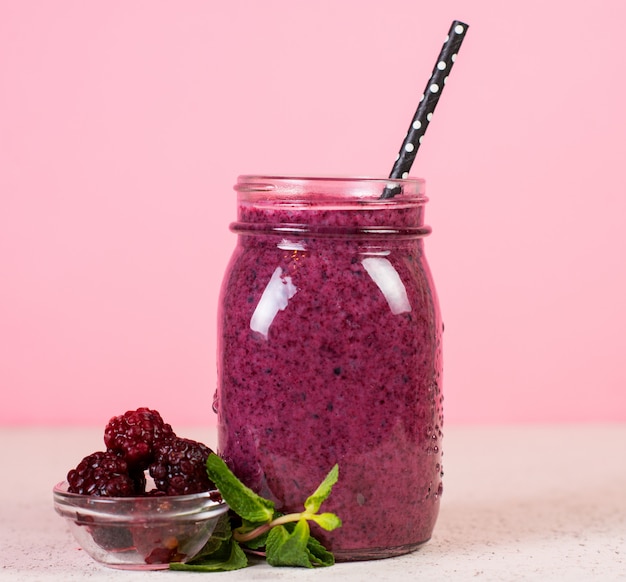 Ein glas frischer beeren-smoothie aus blaubeeren und brombeeren auf einem rosa hintergrund.