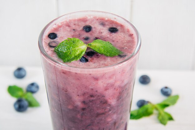 Ein Glas gesunder Blaubeer- und Bananen-Smoothie auf weißem Holzhintergrund mit Minze verziert. Nahaufnahme