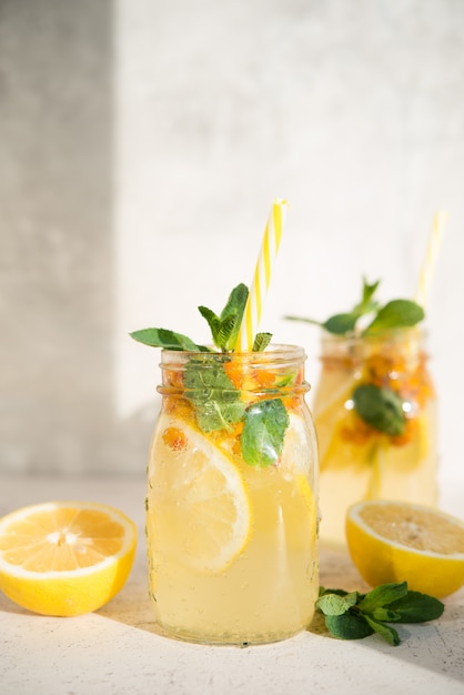 Ein Glas hausgemachte Limonade mit Zitrone, Beeren und Minze auf hellem Hintergrund, Sonnenlicht