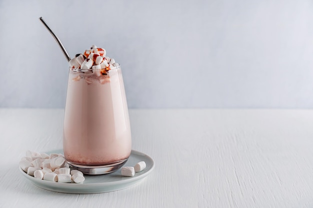 Ein Glas hausgemachter Kakaomilchshake mit Marshmallow- und Sirupgarnitur, serviert auf einem weißen Tisch