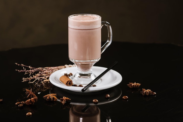 Ein Glas heißen Cappuccino mit Zutaten auf schwarzem Hintergrund