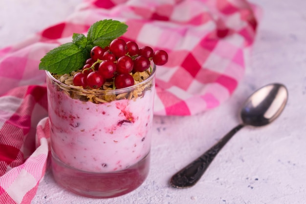 Ein Glas Joghurt mit Müsli und roten Johannisbeeren auf weißem Hintergrund