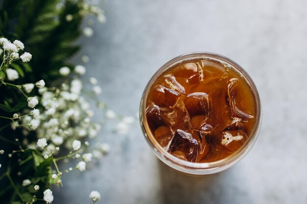 Foto ein glas kalter eiskaffee mit blumenzweigen auf grauem hintergrund, von oben geschossen