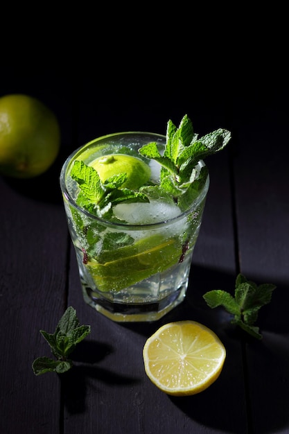 Ein Glas kalter Mojito mit Limette, Zitrone und Minze auf schwarzem Holzhintergrund Nahaufnahme eines erfrischenden Cocktails