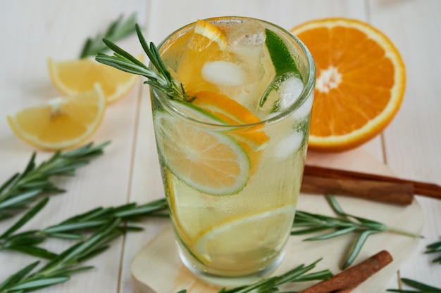 Ein Glas kühle Limonade mit Zitrusfrüchten und Rosmarin, Zimt auf einem Holztisch