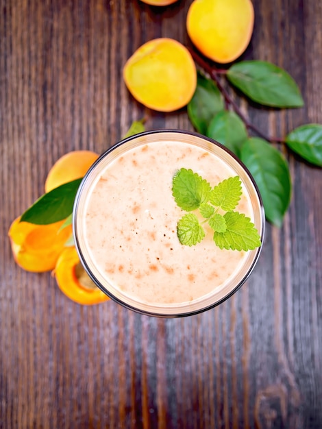 Ein Glas Milchshake mit Aprikosen, Minze auf einem Holzbrett-Hintergrund