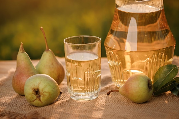 Ein Glas mit Birnensaft und Korb mit Birnen auf Holztisch mit natürlichem Obstgartenhintergrund bei Sonnenuntergang Vegetarische Fruchtzusammensetzung