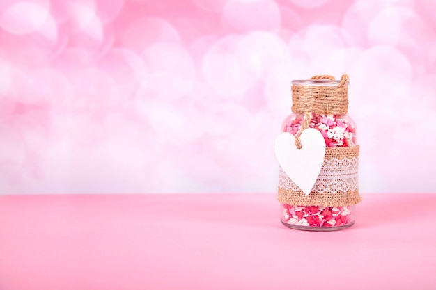 Ein Glas mit bunten Herzen auf einem rosa Hintergrund mit Bokeh