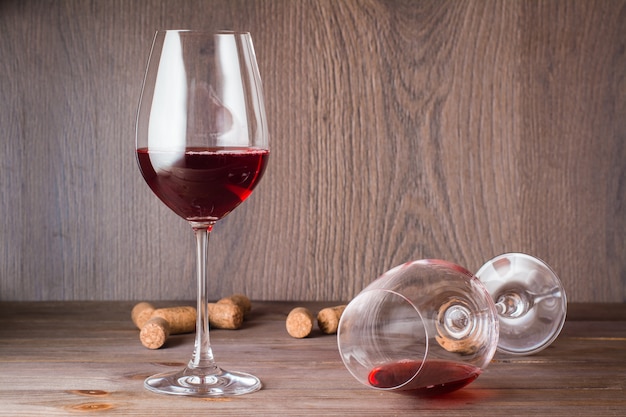 Ein Glas mit den Resten des Rotweins liegt, das andere steht mit Rotwein und Korken gefüllt auf einem Holztisch