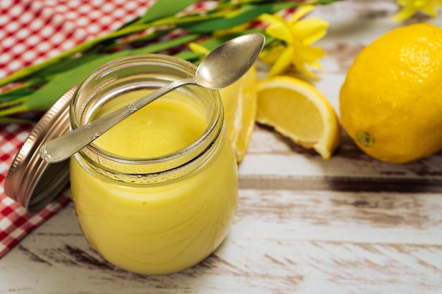 Ein Glas mit hausgemachtem Lemon Curd neben einigen Zitronen auf einem alten Holztisch. Hohe Aussicht.