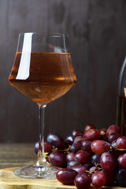 Ein Glas mit Roséwein und ein paar rote Trauben sind in der Nähe. Nahansicht. Vertikale Ausrichtung