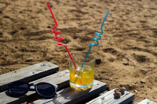 Ein Glas Orangensaft, ein Cocktail, eine Sonnenbrille am Strand