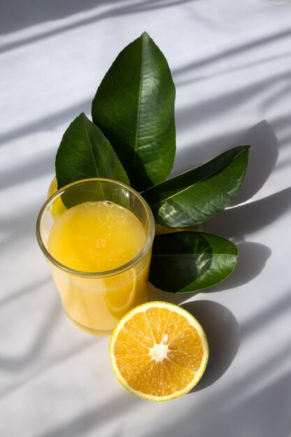 Ein Glas Orangensaft mit Blättern des Baumes und die Hälfte einer Orange mit weißem Hintergrund